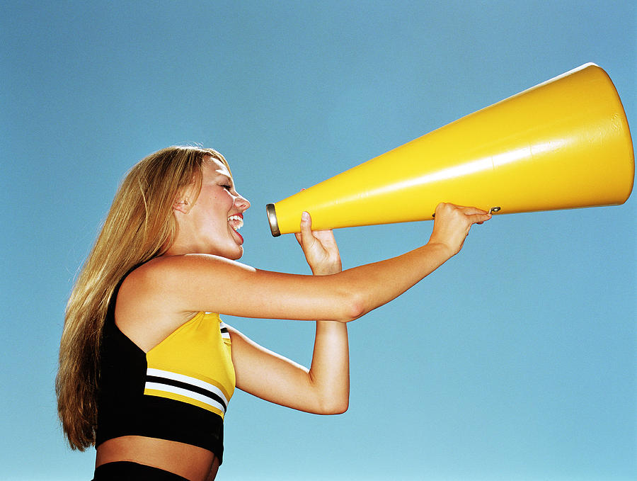 Cheerleader yelling through megaphone, low angle, side view Photograph by Mike Powell