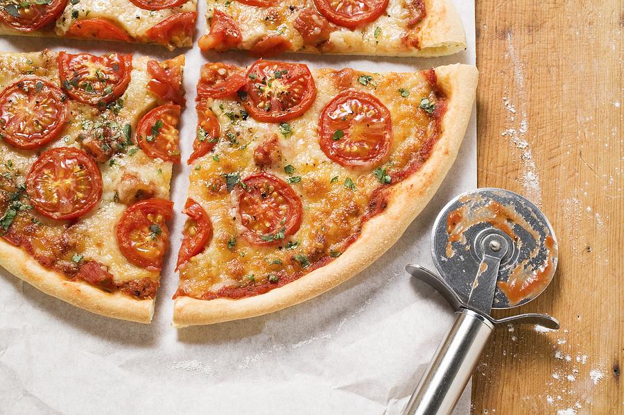 Cheese and tomato pizza with oregano (quartered) Photograph by Foodcollection
