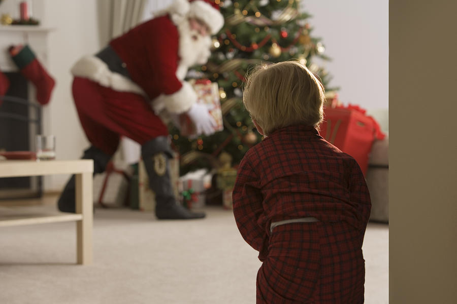 Child peeking at santa claus Photograph by Comstock Images