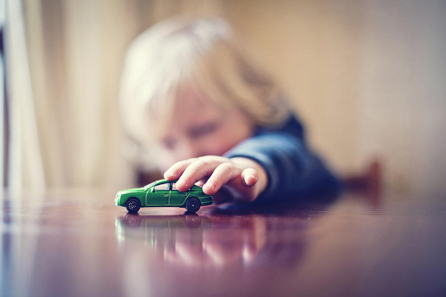 Child playing with toy car Photograph by Sally Anscombe