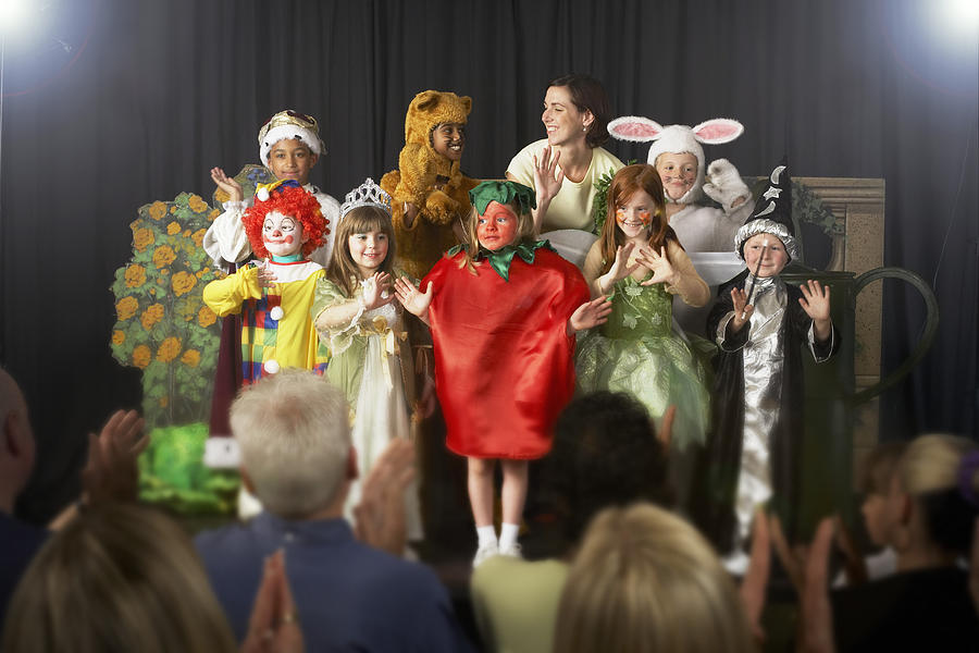 Children (4-9) wearing costumes and teacher waving on stage Photograph by Richard Lewisohn