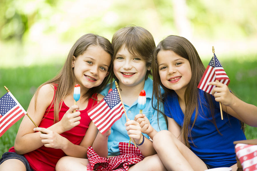 Children enjoy July 4th picnic in summer. American flags, popsicles. Photograph by Fstop123