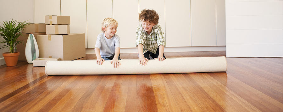 Children unrolling carpet in new house Photograph by Martin Barraud