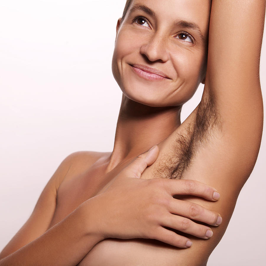 Close-up of a smiling nude woman covering her breast with her hand; her armpit unshaven. Photograph by Thinkstock