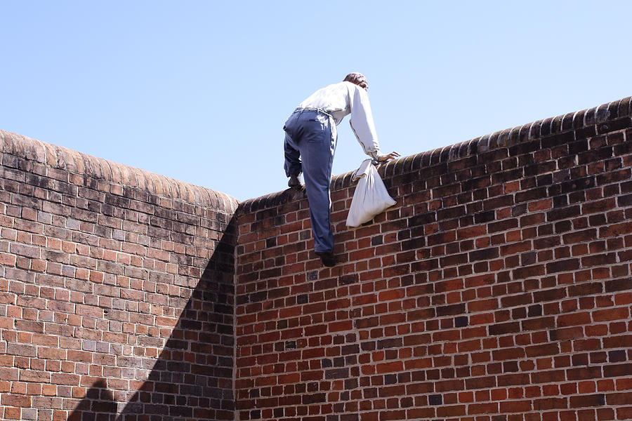 Close-up of a thief climbing over a brick wall Photograph by Claylib