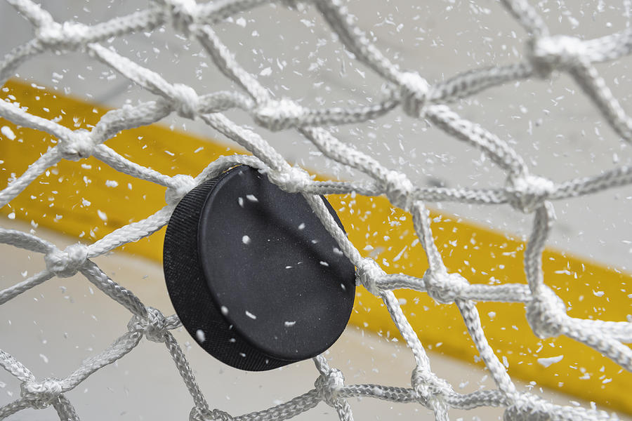 Close-up of an Ice Hockey puck hitting the back of the net as snow flies, front view Photograph by Cmannphoto