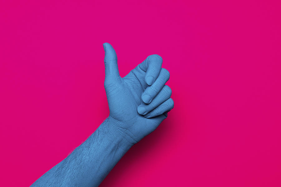 Close-up of blue painted hand gesturing thumb up against pink background Photograph by Norman Posselt