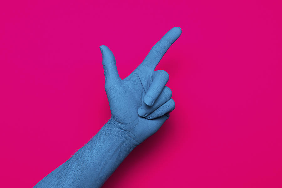 Close-up of blue painted hand pointing against pink background Photograph by Norman Posselt