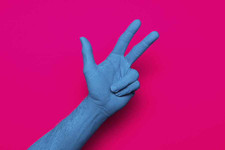Close-up of blue painted hand showing peace sign against pink background Photograph by Norman Posselt