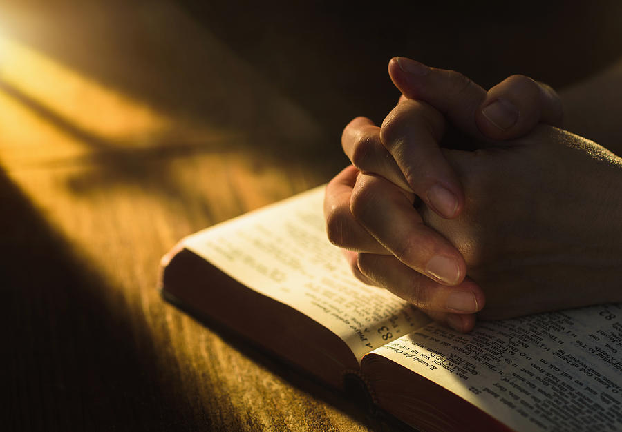 Close up of hands clasped on open Bible Photograph by Tetra Images