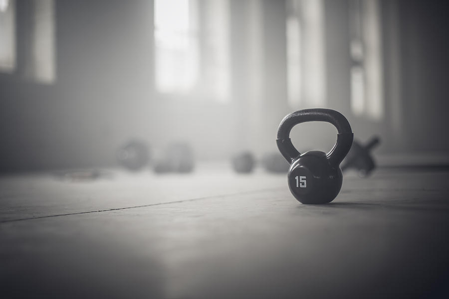 Close up of kettlebell weights on floor of dark gym Photograph by John Fedele