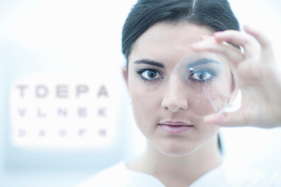 Close up of optician holding lens in eye clinic Photograph by Zero Creatives