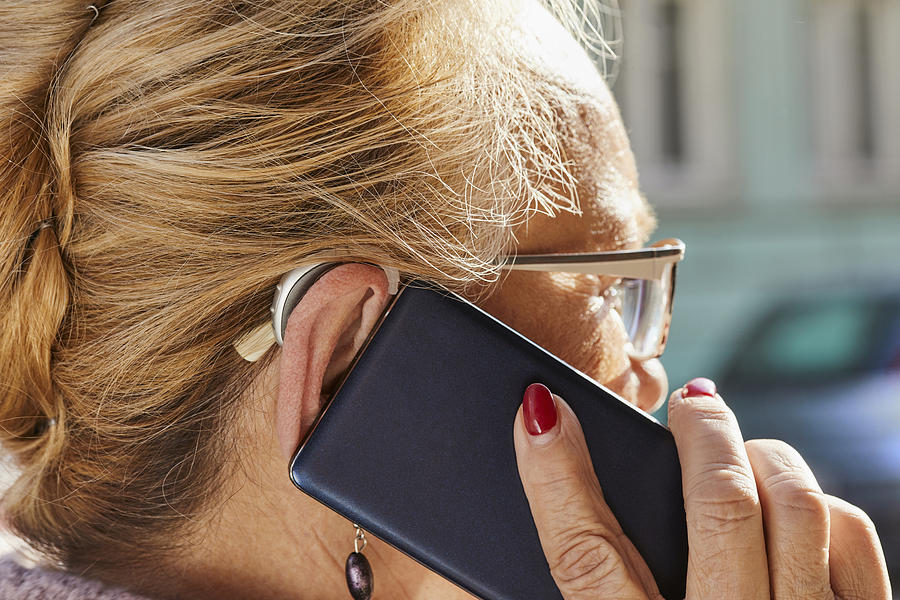 Close-up of senior woman with hearing aid using smartphone Photograph by Westend61