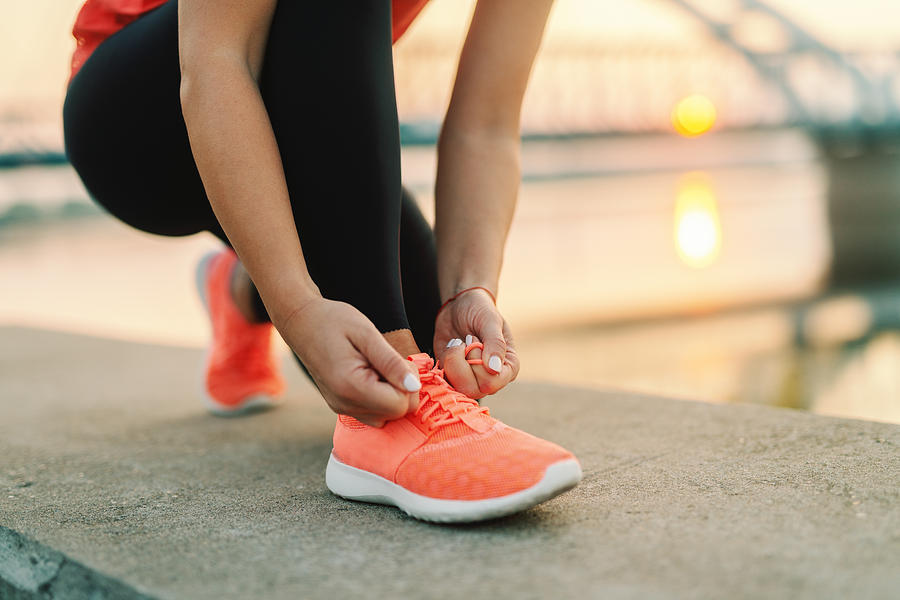 Close up of sporty woman tying shoelace while kneeling outdoor, In background bridge. Fitness outdoors concept. Photograph by Dusanpetkovic