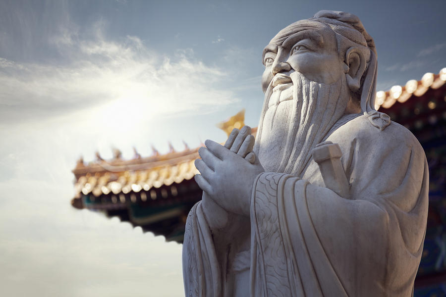 Close-up of stone statue of Confucius, pagoda roof in the background Photograph by XiXinXing