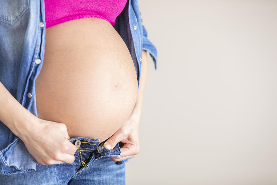 Close up of the big baby bump of a woman trying to close her jeans, Italy Photograph by Giacomo Augugliaro