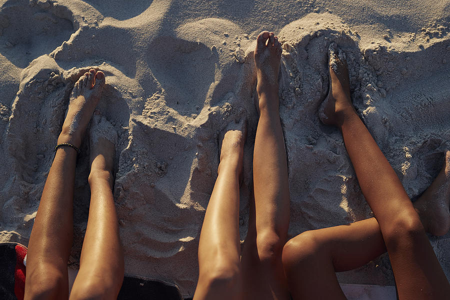Close-up of three young womens legs, on sandy beach Photograph by Klaus Vedfelt
