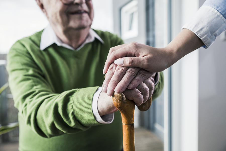 Close-up of woman holding senior mans hand leaning on cane Photograph by Westend61