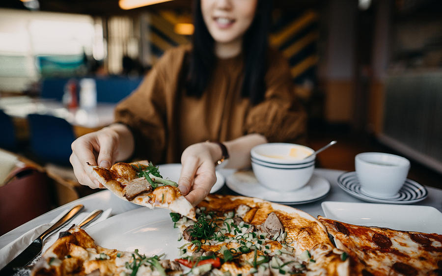 Close up of young woman enjoying meal and eating freshly made pizza in a restaurant Photograph by D3sign
