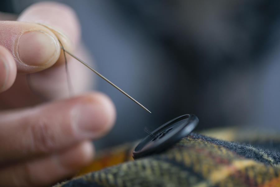 Close up seamstress fingers sewing button onto tartan in workshop Photograph by Atli Mar Hafsteinsson