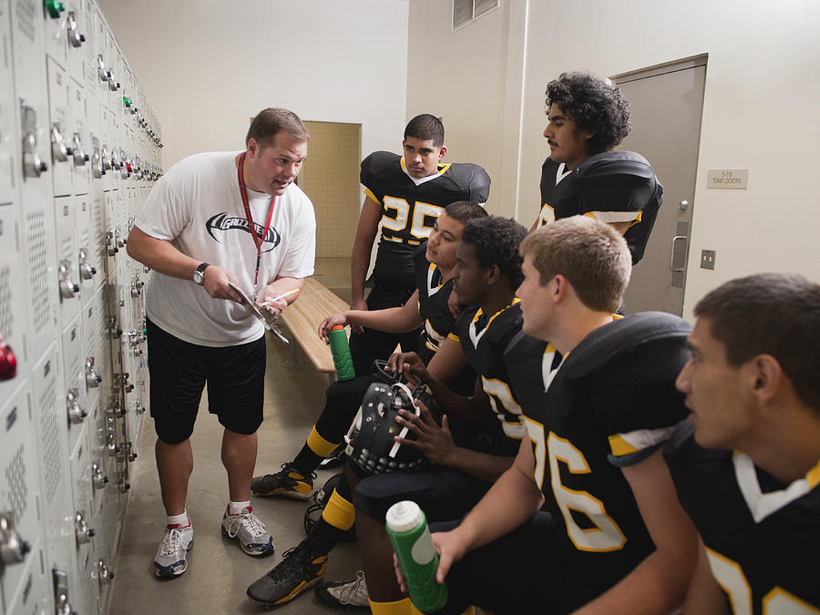 Coach talking to football players in locker room Photograph by Erik Isakson