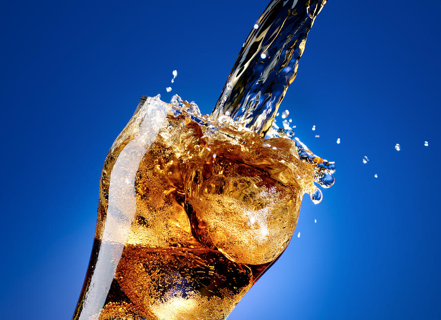 Cola with a large splash, isolated on blue Photograph by Burwellphotography