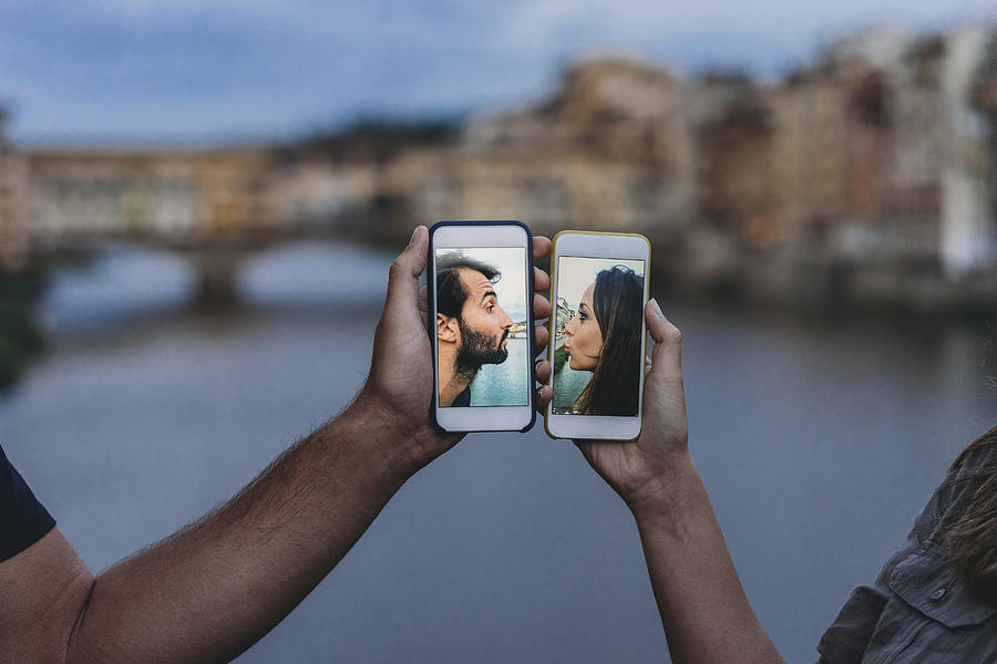Conceptual shot of a young adult couple kissing via mobile phone Photograph by FilippoBacci