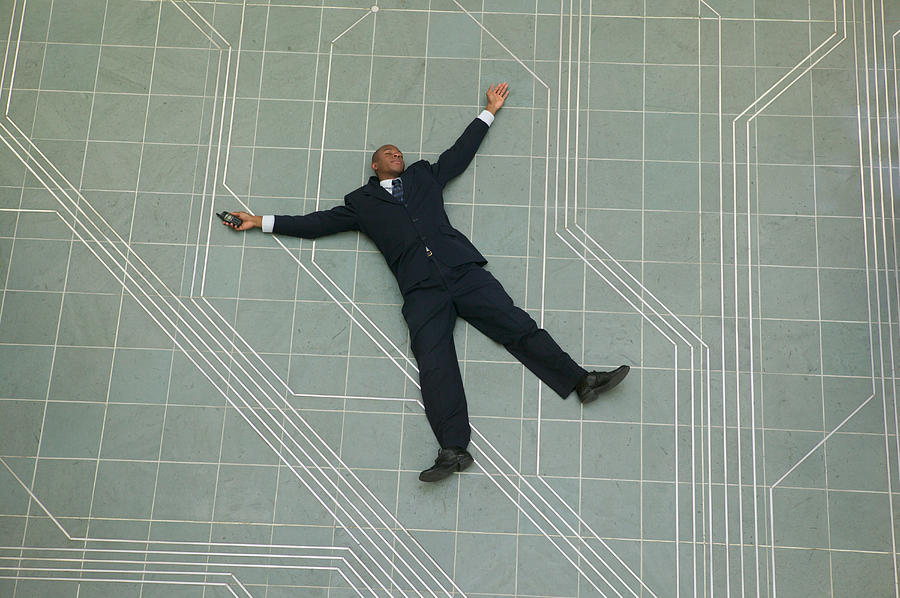 Conceptual Shot Of An African American Business Man As He Lays Flat On The Ground Holding His Phone Photograph by Photodisc