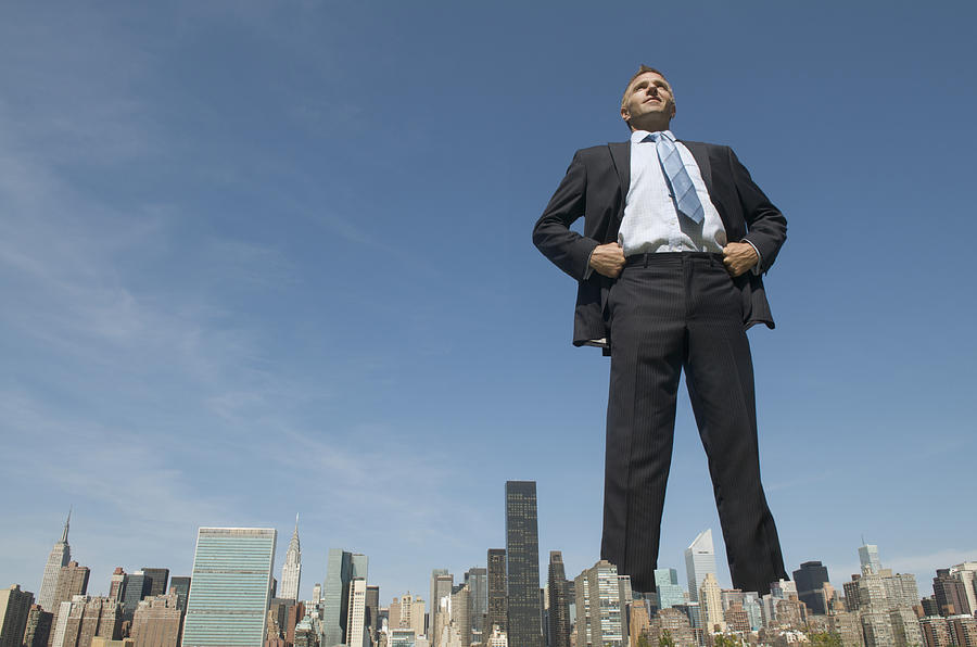 Confident Businessman Giant Towering Over City Skyline Photograph by PeskyMonkey