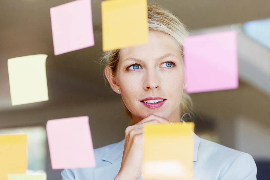 Contemplative business woman with sticky notes on glass window Photograph by GlobalStock