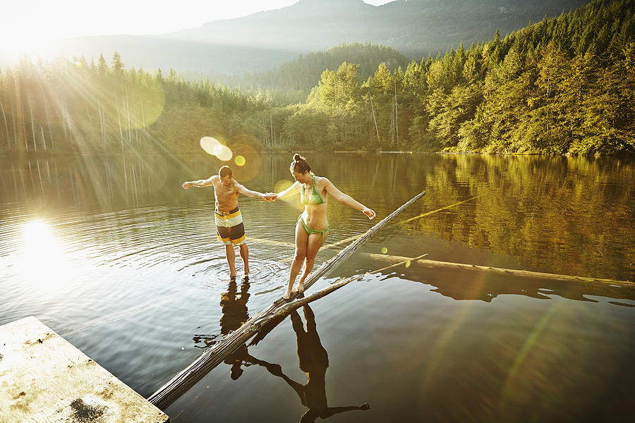 Couple balancing on logs in lake Photograph by Thomas Barwick