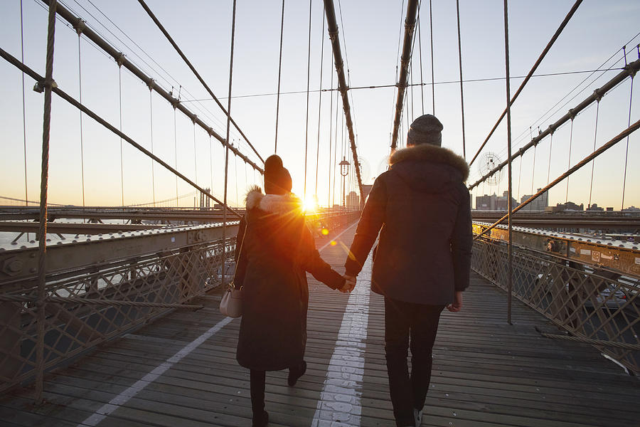 Couple in winter clothing holding hands on Brooklyn Bridge at sunset Photograph by Chris Tobin