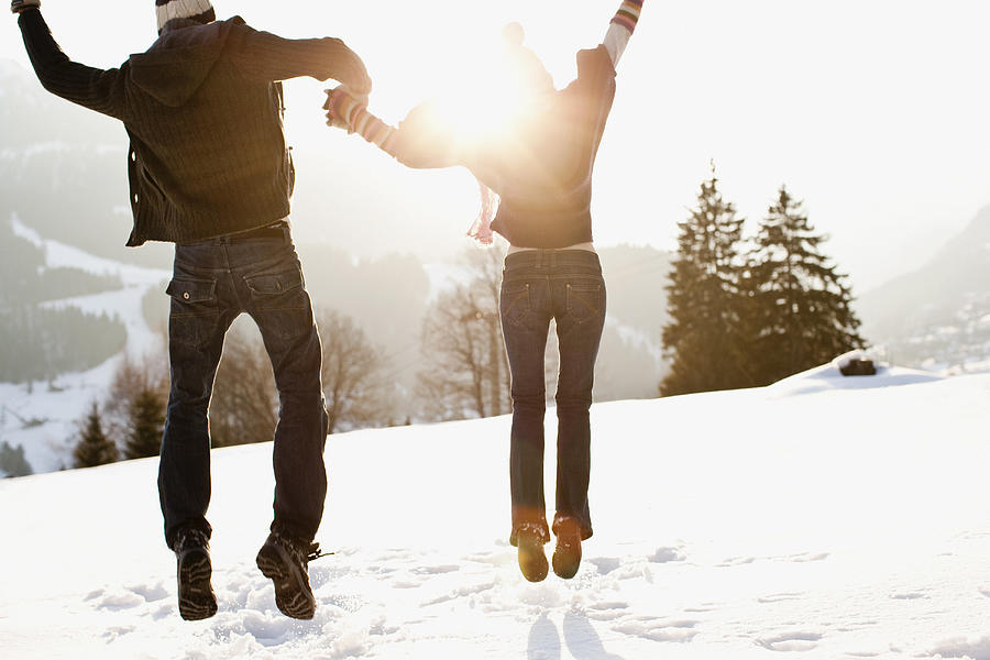 Couple jumping outdoors in snow Photograph by Sam Edwards
