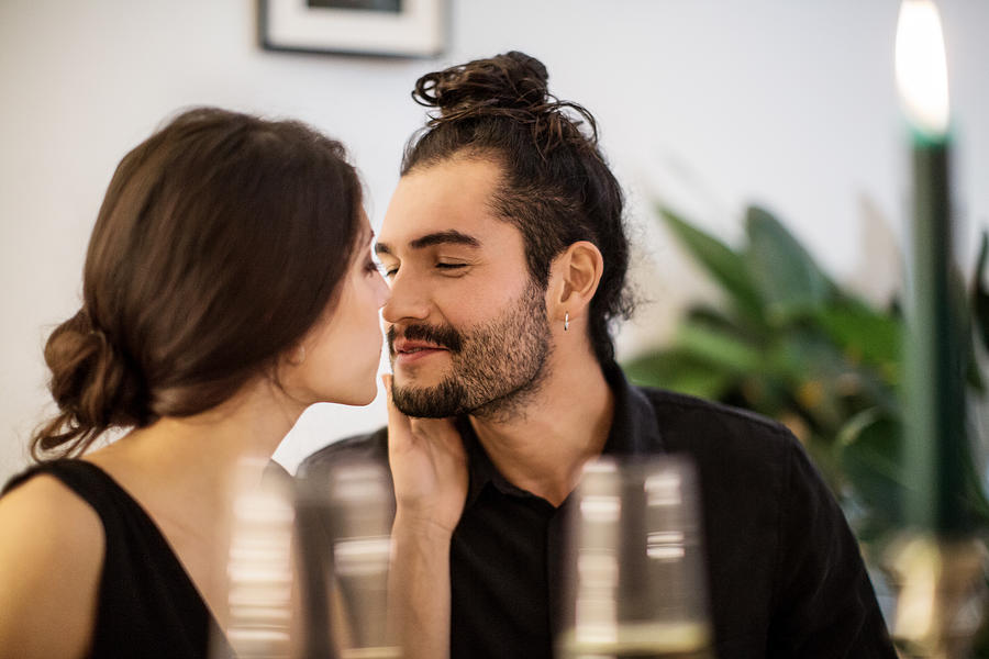 Couple kissing during dinner party at home Photograph by Luis Alvarez