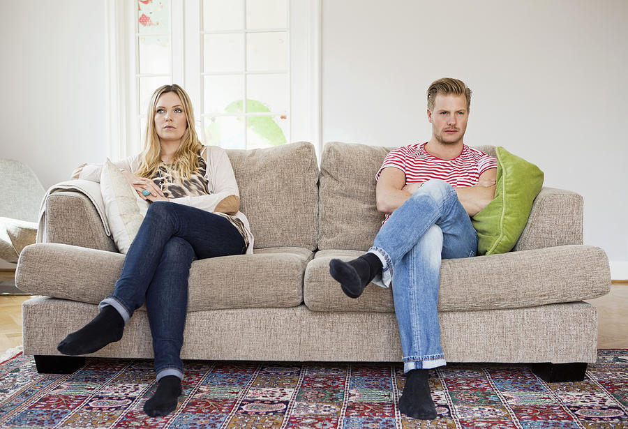 Couple looking away while sitting on sofa with arms folded Photograph by Maskot