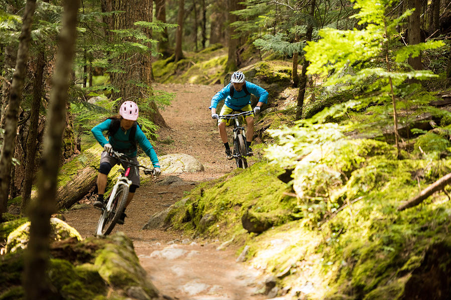 Couple mountain biking through a forest Photograph by stockstudioX