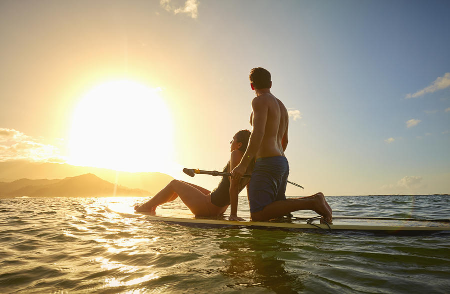 Couple on paddleboard in ocean at sunset Photograph by Colin Anderson Productions Pty Ltd