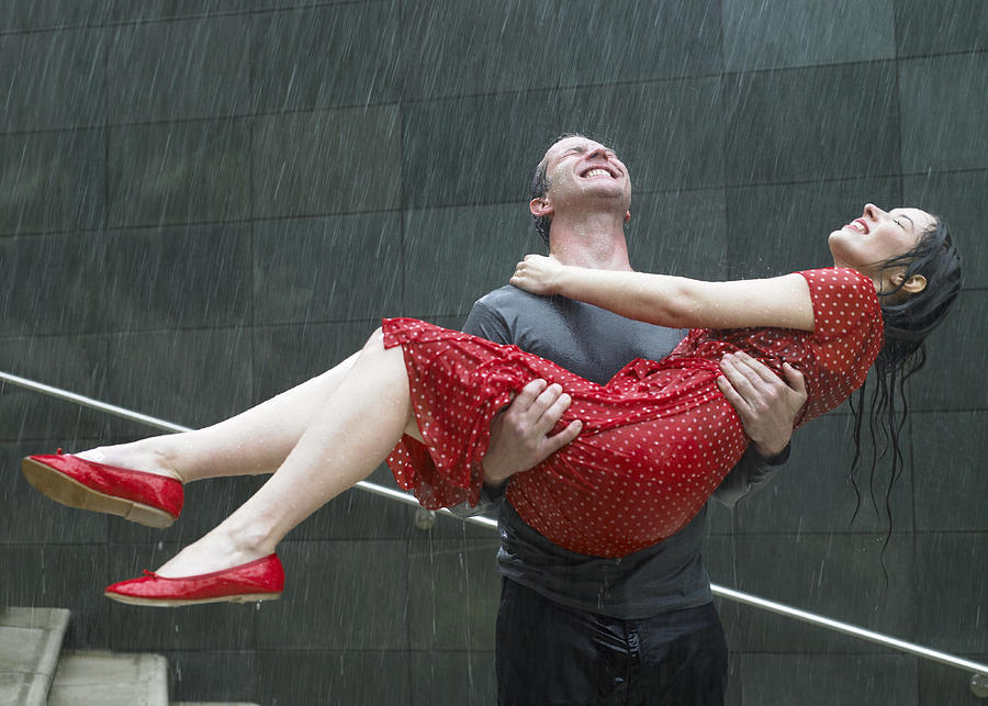 Couple on steps in rain, man carrying young woman, eyes closed Photograph by Michael Blann