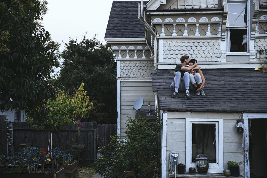 Couple sitting on roof kissing Photograph by Westend61