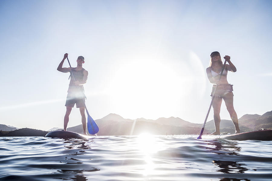 Couple standing on paddleboards in river Photograph by Kolostock
