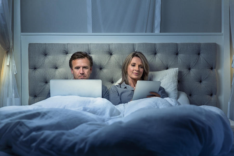 Couple using digital tablet and laptop on bed Photograph by Portra Images