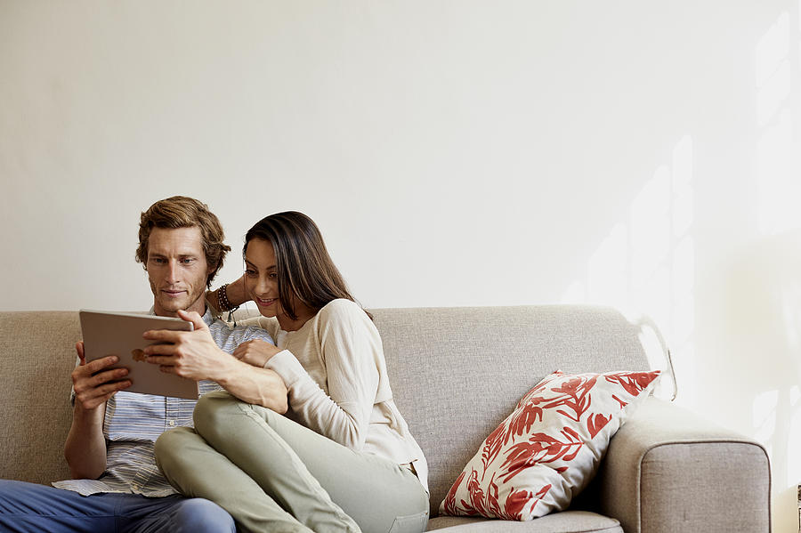 Couple using digital tablet on sofa at home Photograph by Morsa Images