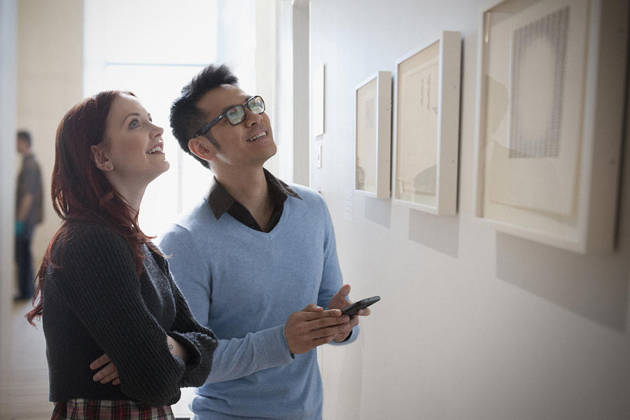 Couple with cell phone admiring artwork in gallery Photograph by Jose Luis Pelaez Inc