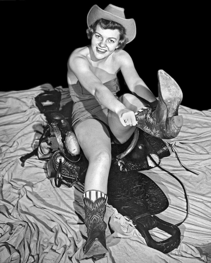 Black And White Photograph - Cowgirl Pulls On Her Boots by Underwood Archives