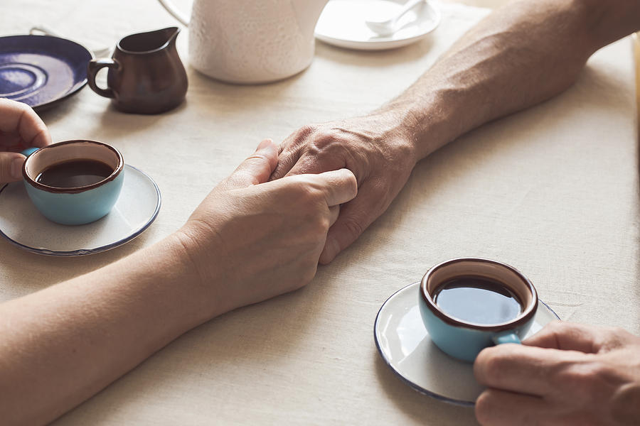Cropped image of senior couple holding hands and drinking coffee Photograph by Istetiana