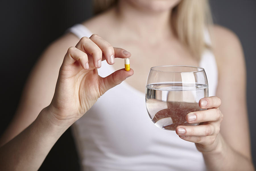 Cropped shot of young woman holding medicine capsule and glass of water Photograph by Maria Fuchs