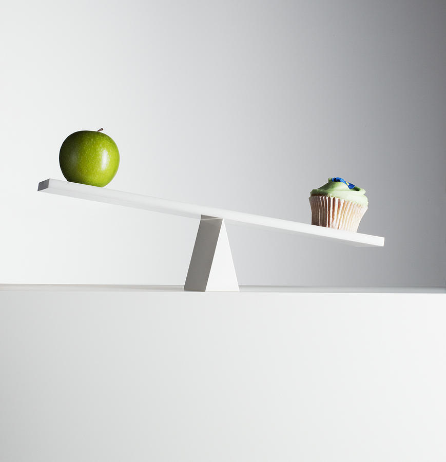 Cupcake tipping seesaw with green apple on opposite end Photograph by Martin Barraud