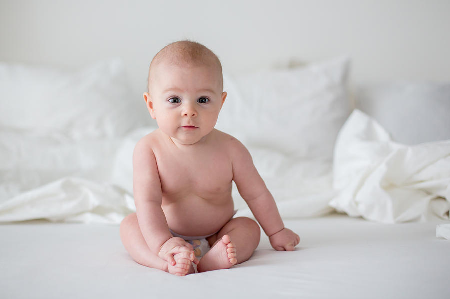 Cute little baby boy in diaper, smiling at camera in white bedroom, cute toddler sitting on bed, smiling Photograph by Tatyana Tomsickova Photography
