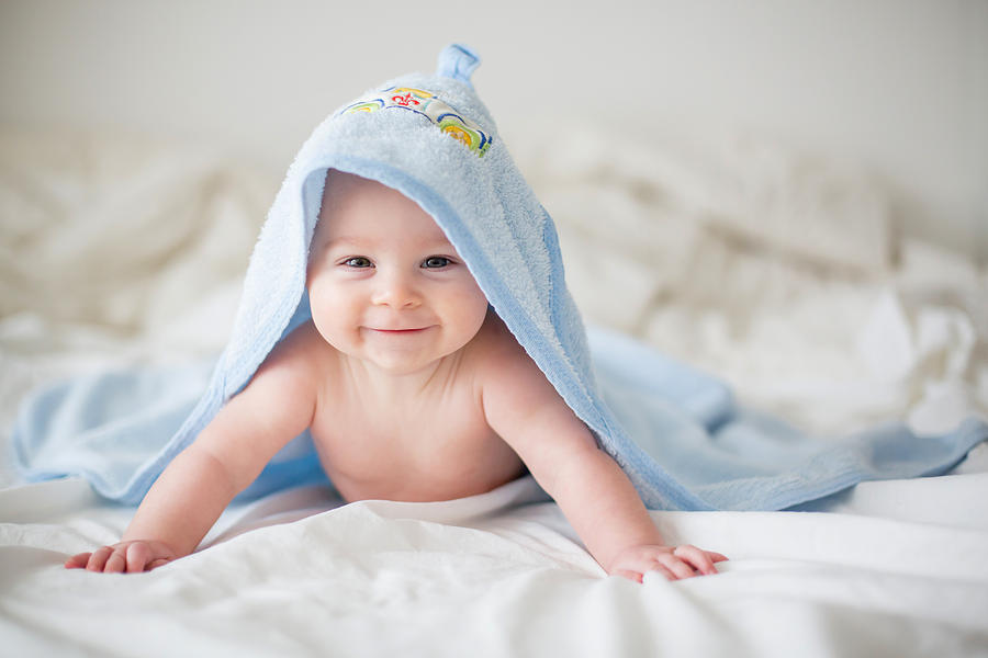 Cute little baby boy, relaxing in bed after bath, smiling happily Photograph by Tatyana_tomsickova