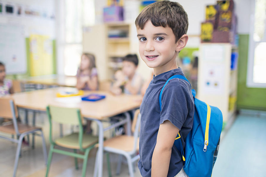Cute schoolboy carrying backpack in classroom Photograph by Xavierarnau